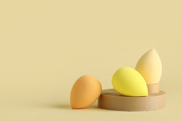 Decorative podiums with makeup sponges on yellow background