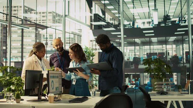 Multiethnic coworkers looking over revenue figures on tablet in diverse office. Multiracial colleagues doing brainstorming, comparing company statistical numbers, working hard to finish job, camera B
