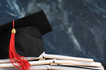 Mortar board with open books on blue background, closeup