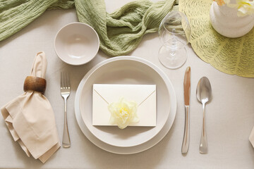 Elegant table setting with beautiful narcissus flower and envelope in bowl, closeup