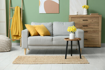 Cozy sofa with dresser, coffee table and narcissus flowers against green wall in living room