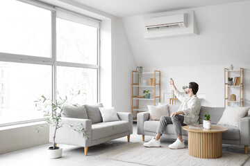 Young man turning on air conditioner in living room