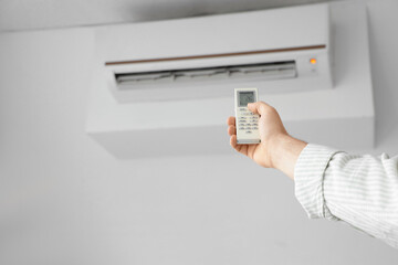 Male hand turning on air conditioner in room, closeup
