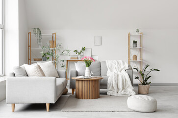 Obraz premium Interior of light living room with grey sofas, shelf units and plants