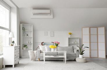 Interior of light living room with grey sofa, table and spring flowers