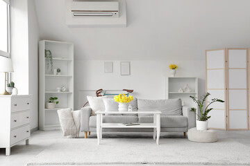 Interior of light living room with grey sofa, table and daffodils in vases