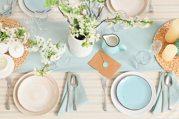 Elegant table setting with plates, envelope and blooming tree branches, top view