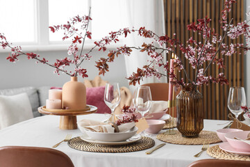 Elegant table setting with plates, burning candles and blooming tree branches