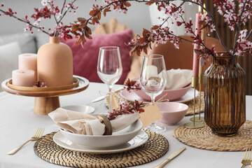 Elegant table setting with plates, burning candles and blooming tree branches