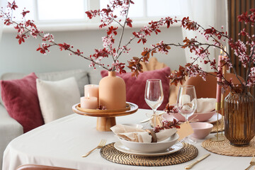 Elegant table setting with plates, burning candles and blooming tree branches