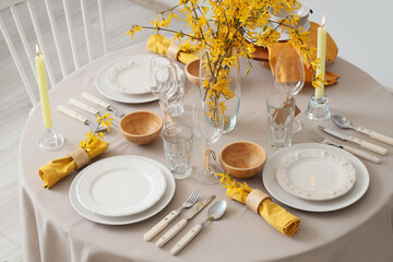 Elegant table setting with clean plates, burning candles, cutlery and blooming tree branches