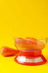 Kitchen scale with fresh carrots on yellow background, space for text