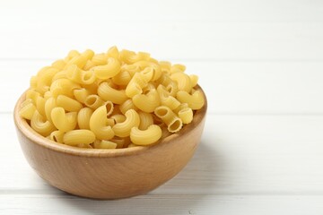 Raw horns pasta in bowl on white wooden table, closeup