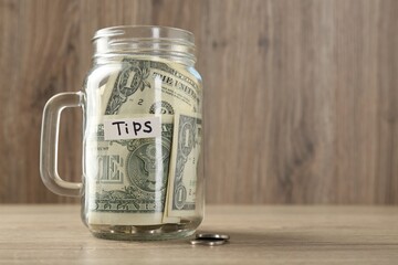 Mason jar with tips on wooden table, closeup. Space for text
