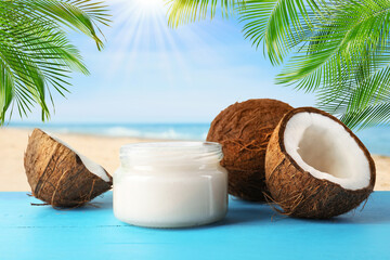 Cooking oil in jar and coconuts on blue table against beach