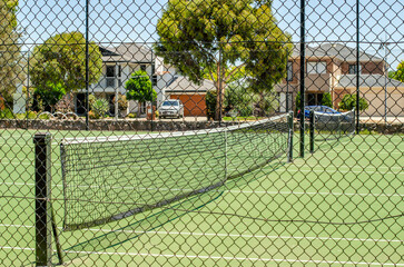 A public tennis court enclosed by a chain-link fence in a residential neighborhood in Australia surrounded by houses and homes. An outdoor sports facility and community amenity. Tarneit, Melbourne