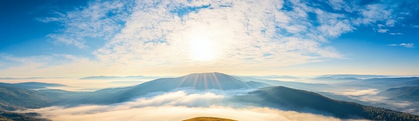 Panoramic view of Carpathian Mountains with foggy valley and sunlight on mountain peak under vibrant blue sky with clouds, wide high-resolution morning landscape background