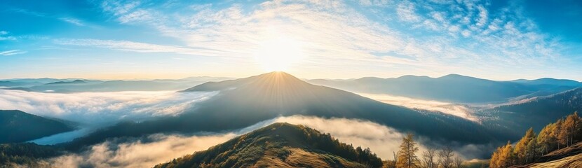 Panoramic view of Carpathian Mountains with foggy valley and sunlight on mountain peak under vibrant blue sky with clouds, wide high-resolution morning landscape background