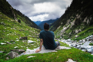 Naklejka premium Male hiker resting during mountain trek in HImachal Pradesh, India overlooking scenic view with rugged peaks surrounding landscape 