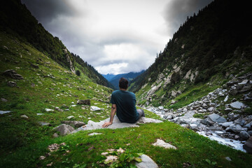 Male hiker resting during mountain trek in HImachal Pradesh, India overlooking scenic view with...