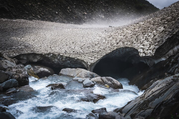 Powerful stream of glacial meltwater flowing through a natural snow tunnel on a Himalayan trekking...