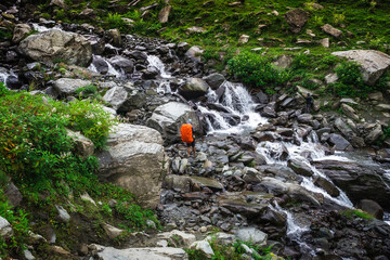 A hiker crossing the waterfall along the trail during his hike in mountains