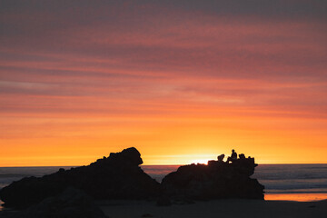 Silhouettes of a person sat on a rock on the beach at sunset