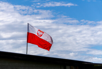 The Polish flag with the national emblem, fluttering against a slightly cloudy sky. The flag was...