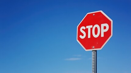 Obraz premium A bright red octagonal stop sign with bold white letters, standing against a clear blue sky