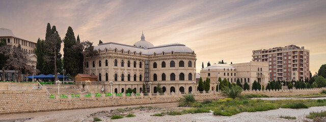 Mahsati Ganjavi Center stands majestically in Ganja, Azerbaijan, highlighted by its distinct domes against a backdrop of a dusky sky. The surrounding area features lush greenery and modern buildings