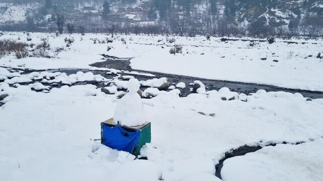 pan up reveal shot showing the frozen lidder river with a snowman perched on the side and the majestic Himalaya mountains rising in the distance