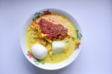 Lontong, a traditional Southeast Asian dish of compressed rice cakes in rich coconut curry, served with lodeh, sambal kacang, sambal tumis, hard-boiled eggs, and fresh vegetables on a decorative plate