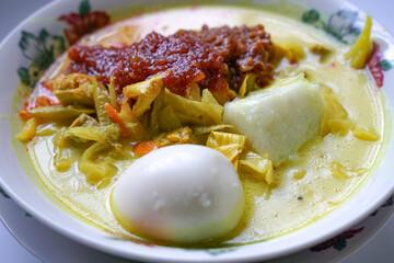 Lontong, a traditional Southeast Asian dish of compressed rice cakes in rich coconut curry, served with lodeh, sambal kacang, sambal tumis, hard-boiled eggs, and fresh vegetables on a decorative plate