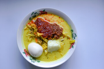 Lontong, a traditional Southeast Asian dish of compressed rice cakes in rich coconut curry, served with lodeh, sambal kacang, sambal tumis, hard-boiled eggs, and fresh vegetables on a decorative plate
