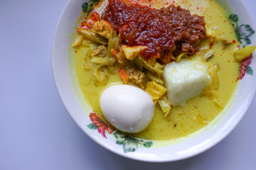 Lontong, a traditional Southeast Asian dish of compressed rice cakes in rich coconut curry, served with lodeh, sambal kacang, sambal tumis, hard-boiled eggs, and fresh vegetables on a decorative plate