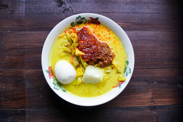 Lontong, a traditional Southeast Asian dish of compressed rice cakes in rich coconut curry, served with lodeh, sambal kacang, sambal tumis, hard-boiled eggs, and fresh vegetables on a decorative plate