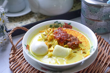 Lontong, a traditional Southeast Asian dish of compressed rice cakes in rich coconut curry, served with lodeh, sambal kacang, sambal tumis, hard-boiled eggs, and fresh vegetables on a decorative plate