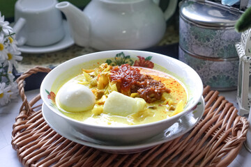 Lontong, a traditional Southeast Asian dish of compressed rice cakes in rich coconut curry, served with lodeh, sambal kacang, sambal tumis, hard-boiled eggs, and fresh vegetables on a decorative plate