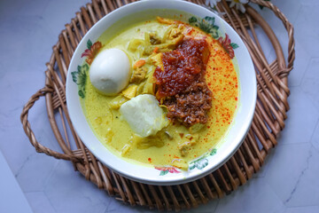 Lontong, a traditional Southeast Asian dish of compressed rice cakes in rich coconut curry, served with lodeh, sambal kacang, sambal tumis, hard-boiled eggs, and fresh vegetables on a decorative plate