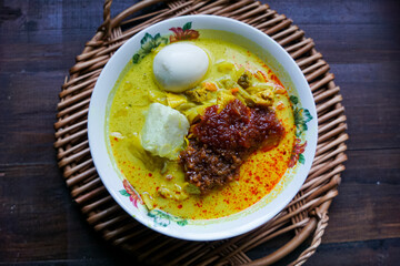 Lontong, a traditional Southeast Asian dish of compressed rice cakes in rich coconut curry, served with lodeh, sambal kacang, sambal tumis, hard-boiled eggs, and fresh vegetables on a decorative plate
