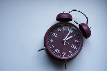 A maroon analog alarm clock with silver legs and twin bells, isolated on white background. 