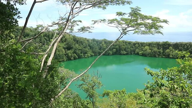 Lake Tolire Besar on Ternate Island, North Maluku seen from the side of the mountain, you can see shady trees and a steep valley leading to the lake, and the blue sea in the distance on a clear day