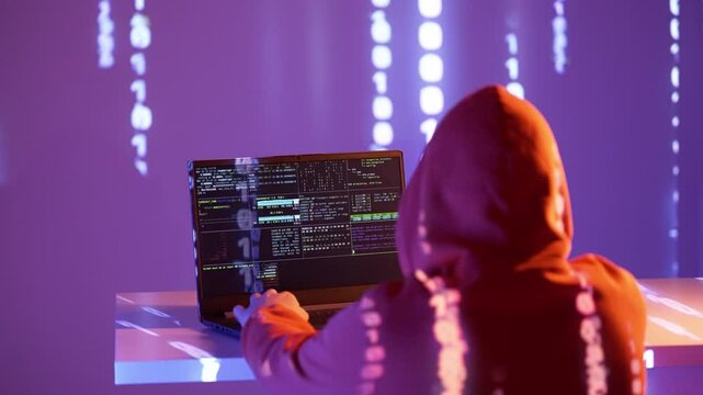 A hooded hacker types on a laptop surrounded by projected binary code and terminal screens. The scene glows with purple neon, emphasizing cybercrime, surveillance, and digital infiltration.