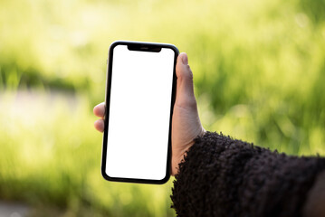 Female hand holding smartphone with blank white screen in the garden – mobile app mockup template