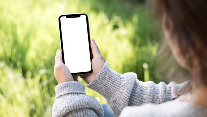 Main féminine tenant un smartphone avec un écran blanc vierge dans le jardin – modèle de maquette d'application mobile Bannière