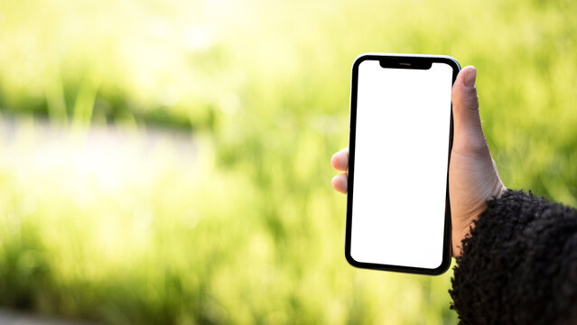 Main f&eacute;minine tenant un smartphone avec un &eacute;cran blanc vierge dans le jardin &ndash; mod&egrave;le de maquette avec incrustation mockup Banni&egrave;re