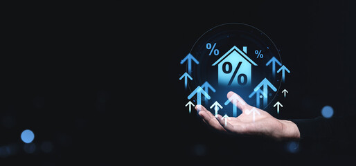 Conceptual image of rising home interest rates with upward arrows and house icon in a hand on a creative background.