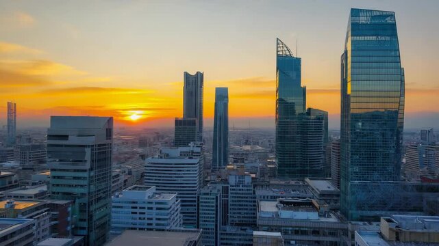 Dramatic sunset casts orange hues over a sprawling generic cityscape filled with modern glass skyscrapers and towers