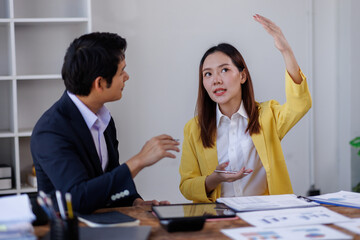 Two happy asian employees working together using computer planning project. business woman consulting teaching young employee looking at laptop sitting at desk in office
