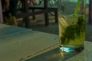 Ice cold mojito cocktail with mint leaves and a straw sitting on a table in an outdoor beach bar